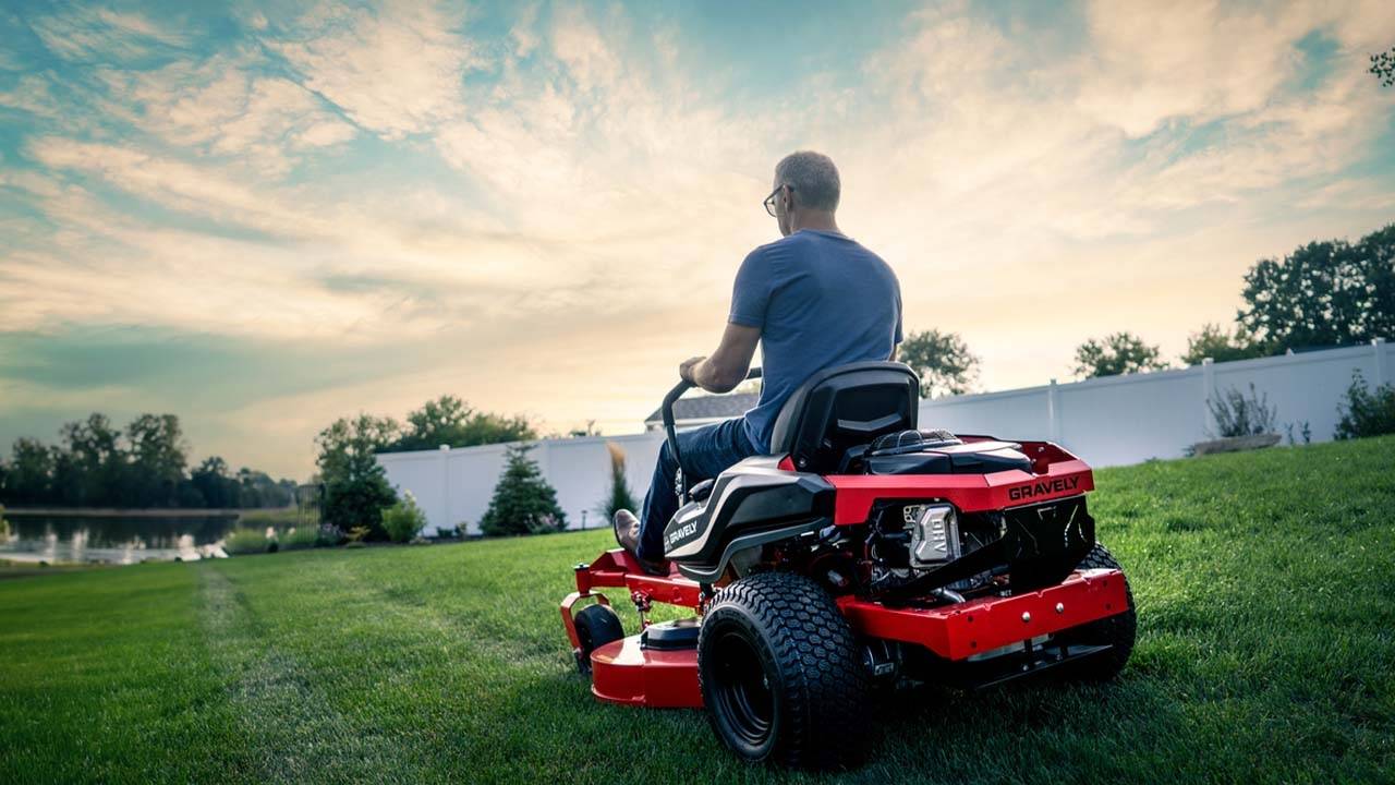 Person mowing green grass with a heavy-duty riding mower.