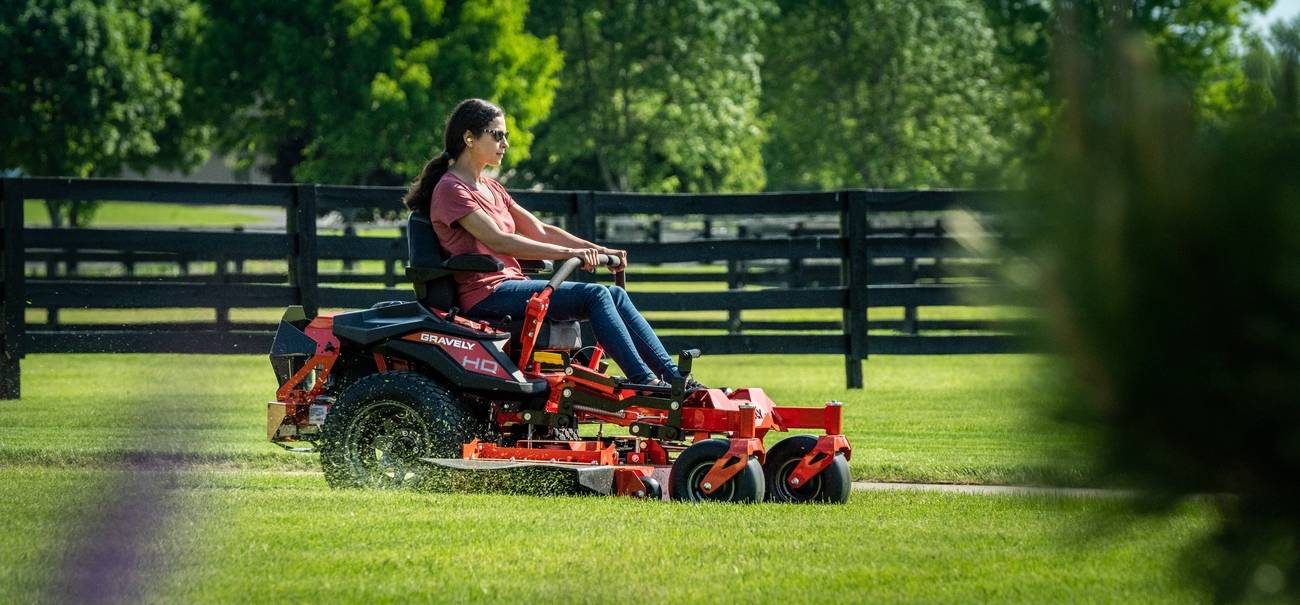 Person mowing green grass with a heavy-duty riding mower.